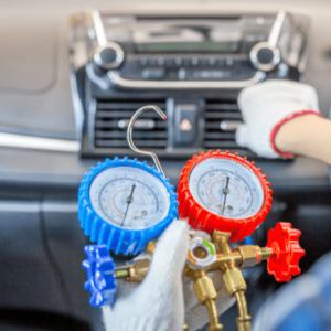 A technician checks a car's AC system with a pressure gauge tool on the dashboard.