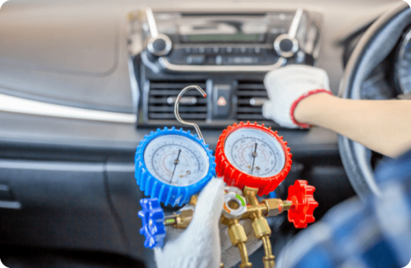 A technician checks a car's AC system with a pressure gauge tool on the dashboard.