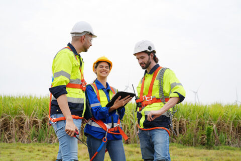 Engineers in safety gear talking in front of wind turbines.