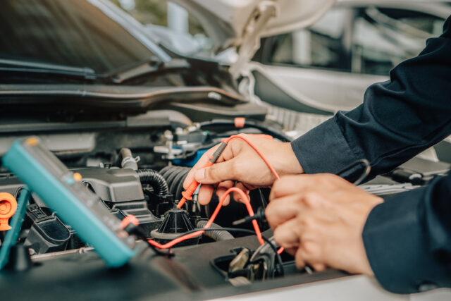 Mechanic testing car engine with multimeter leads