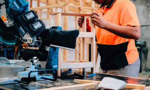 Worker in high-vis shirt assembling a wooden frame in a workshop.