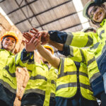 Construction team huddling together in a warehouse.