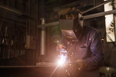 Worker using an angle grinder on metal held in a workshop vise.
