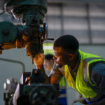 Professional machinist in a safety vest operating a heavy-duty drill press.