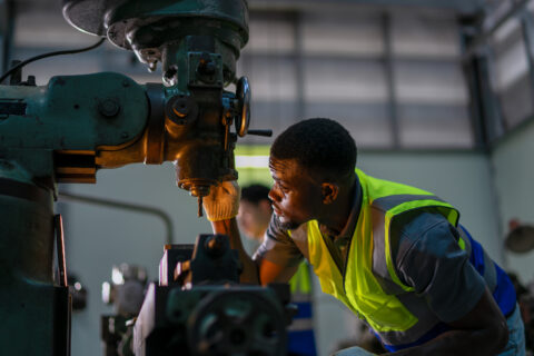 Professional machinist in a safety vest operating a heavy-duty drill press.