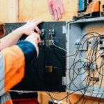 Electrician working on an open electrical panel with many wires.