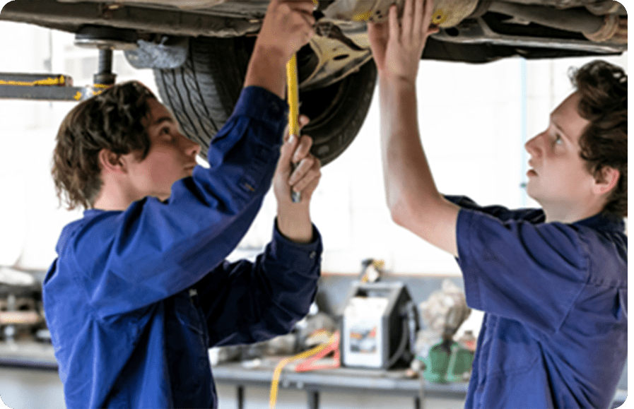 Two apprentices working under a lifted car