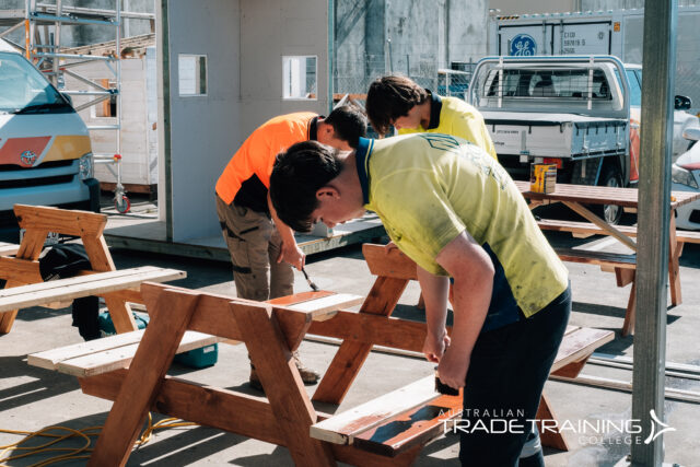 Students painting wooden benches during carpentry training session