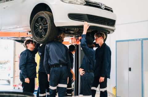 Mechanics in blue uniforms working under a car on a lift.