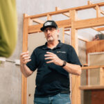 Instructor in a black polo gesturing while teaching in a workshop.