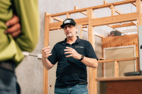 Instructor in a black polo gesturing while teaching in a workshop.