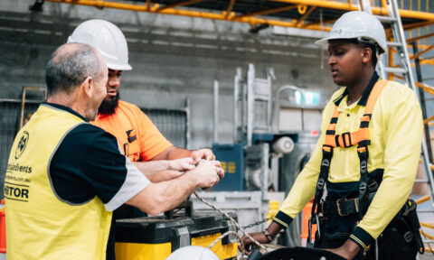 Workers in high-vis gear and hard hats training with a rope.
