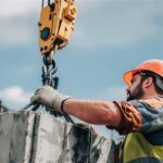 Construction worker rigging a concrete block to a crane hook.