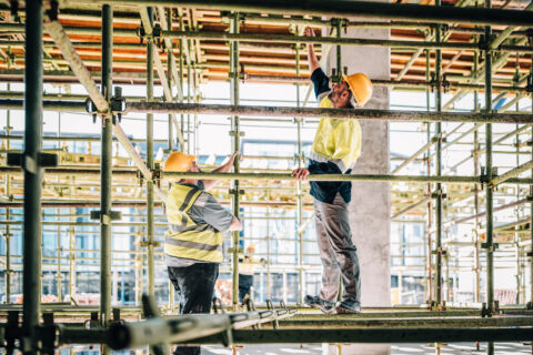 Two workers in high-vis gear assembling scaffolding on a site.