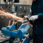 Worker using an angle grinder on metal held in a workshop vise.