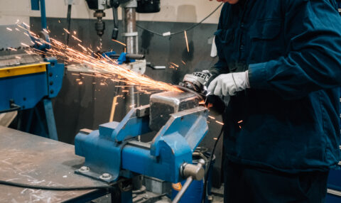 Worker using an angle grinder on metal held in a workshop vise.