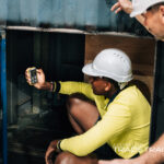Worker in a hard hat using a handheld gas detector in a void.