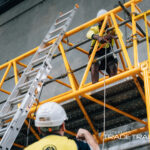 Workers in safety gear training on a yellow scaffolding tower.
