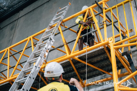 Workers in safety gear training on a yellow scaffolding tower.
