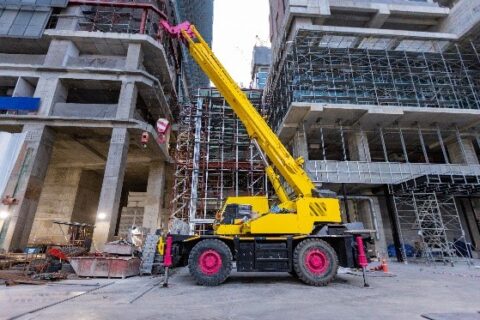 Large yellow mobile crane operating at an urban construction site.
