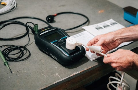 Hands testing a power plug with a portable appliance tester.