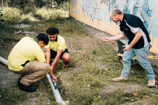 Trainer guiding students measuring a pipe outdoors