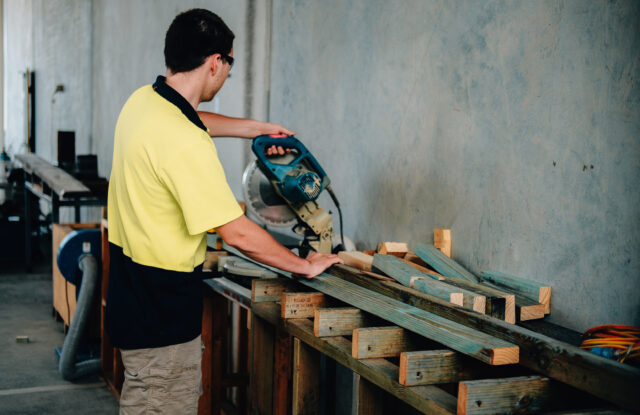 Worker cutting wooden planks using electric saw in carpentry workshop