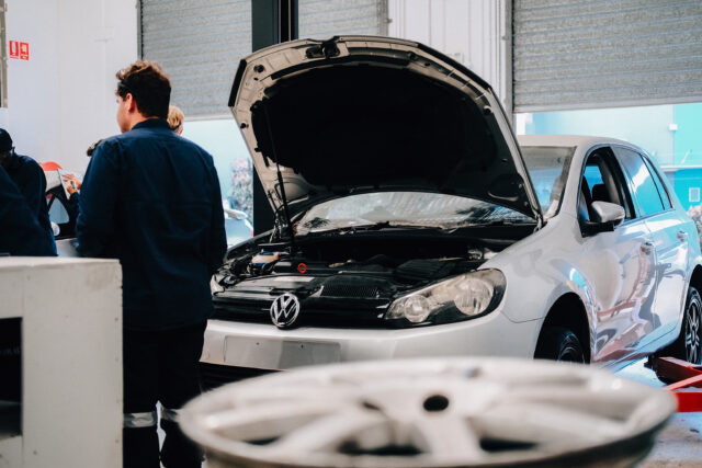 Mechanic student inspecting a car with the hood open.