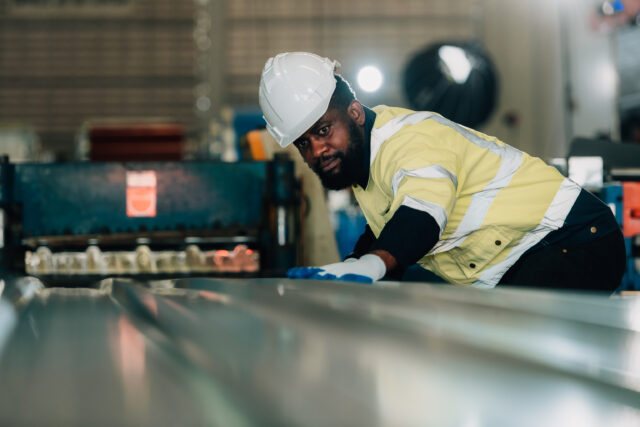 Worker in hard hat inspecting metal sheet