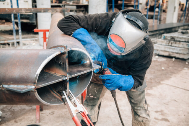 Welder working on large steel pipe outdoors