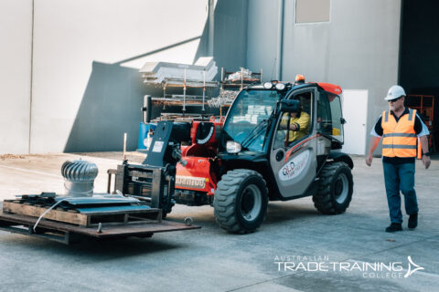 Manitou telehandler moving a pallet with an instructor nearby.