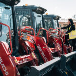 Woman inspecting row of red skid steer loaders