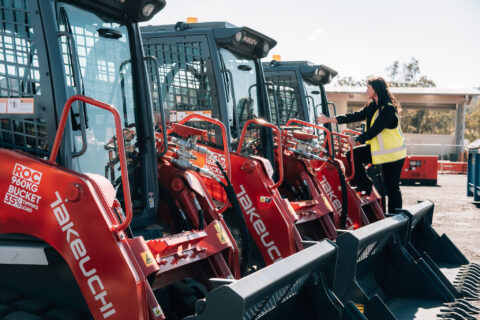 Woman inspecting row of red skid steer loaders